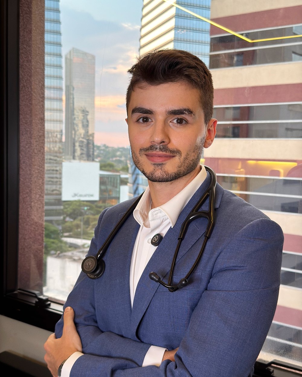 Dr. Pedro Santana, cardiologista, de terno azul com estetoscópio em consultório com vista para São Paulo